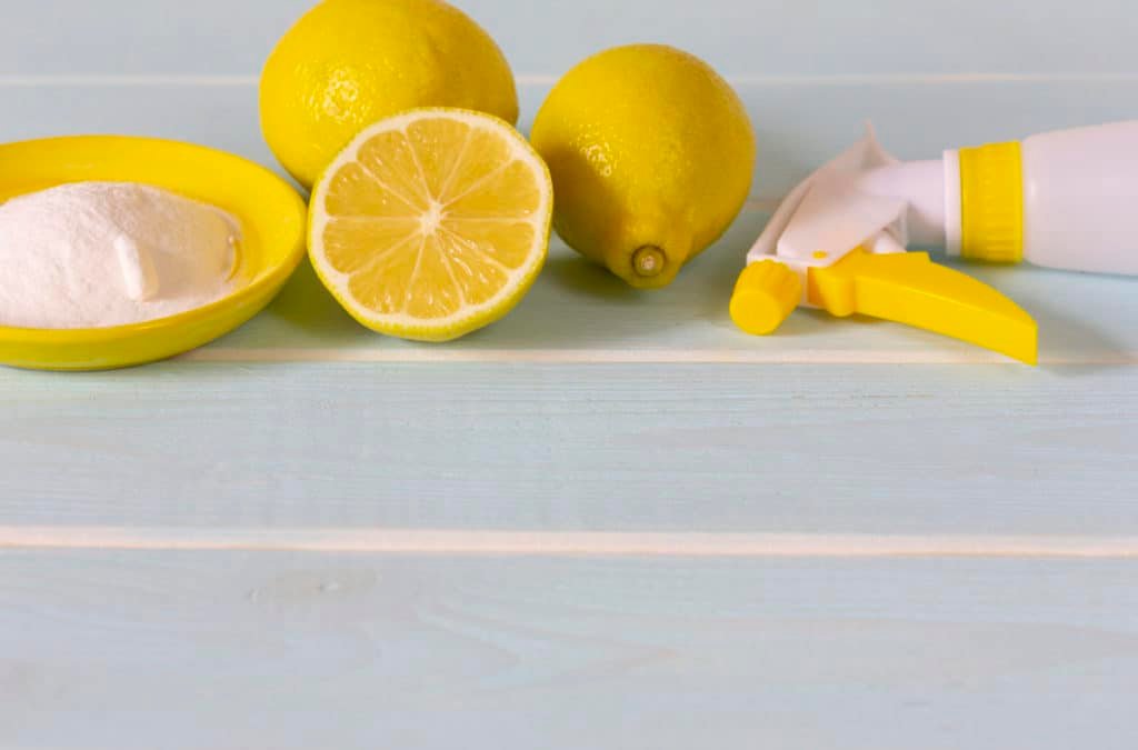 Natural products for eco cleaning. Lemon, baking soda and vinegar for eco housekeeping. All objects, lemon, bowl, pump sprayer are in yellow color. Blue wooden background.